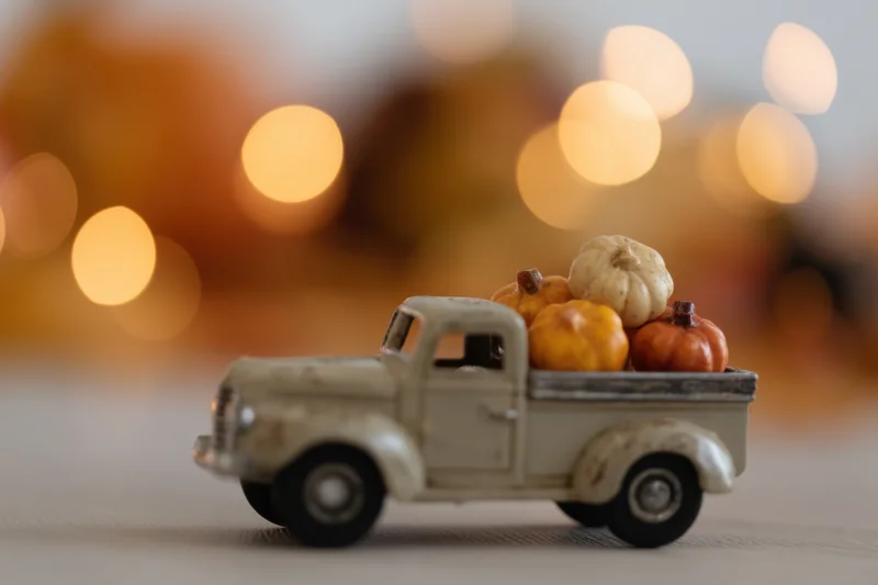 Vintage toy truck carrying small decorative pumpkins on a tabletop with warm bokeh background