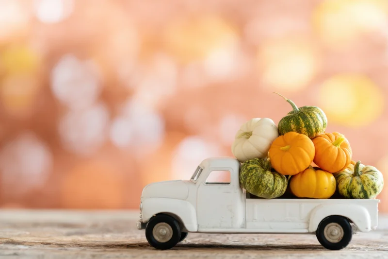 Vintage white toy truck carrying small colorful pumpkins and gourds on wooden surface with bokeh background