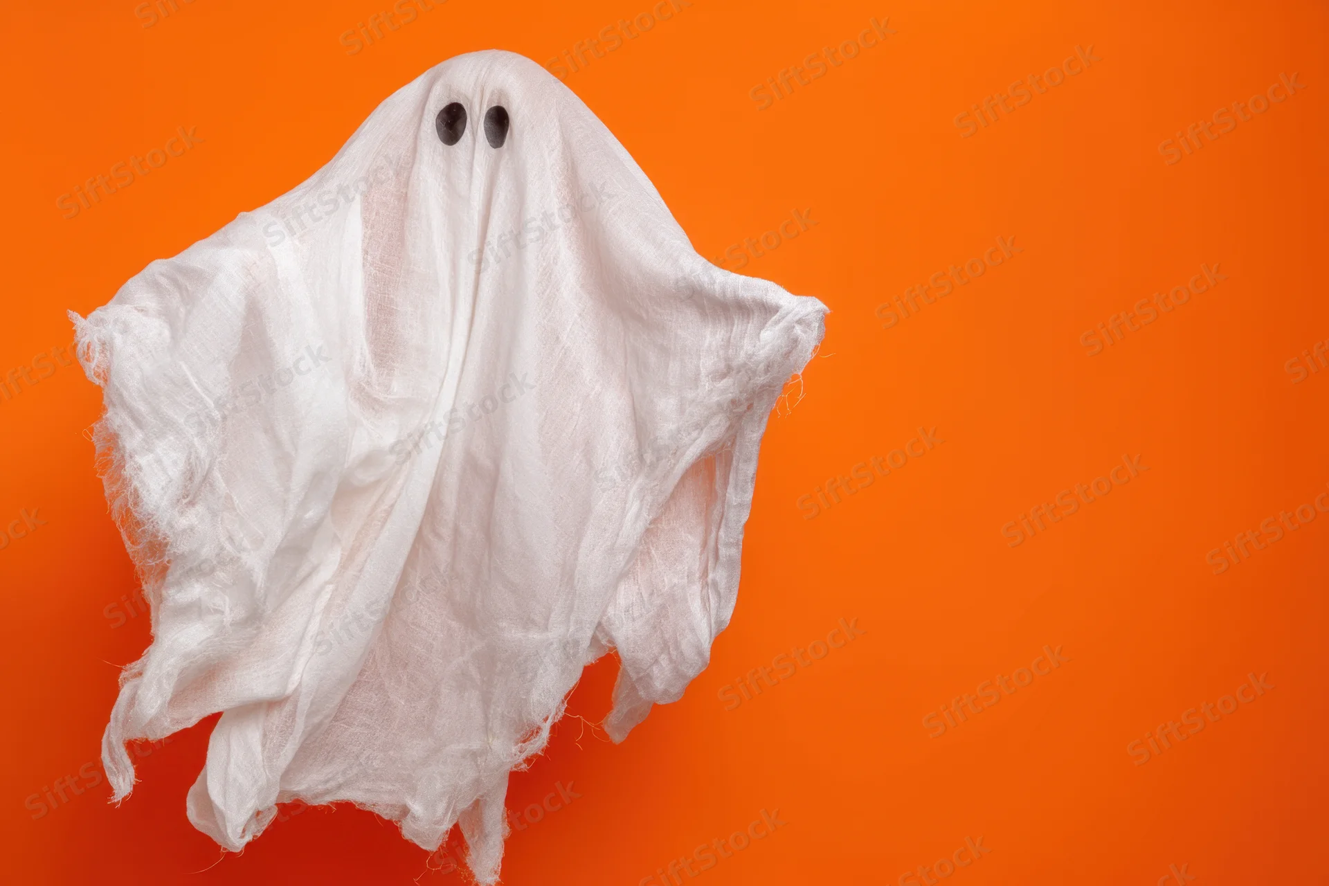 Whimsical ghost made of tattered white sheet floating against orange background
