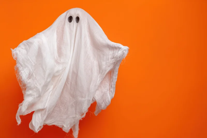 Whimsical ghost made of tattered white sheet floating against orange background