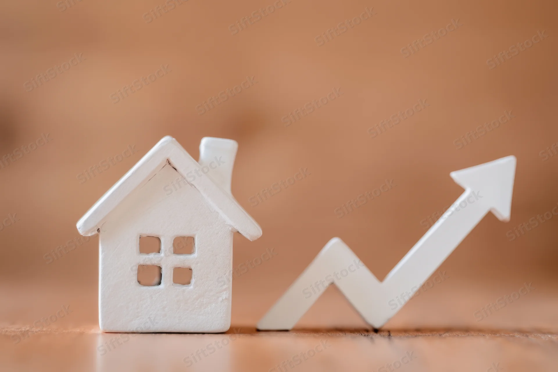White house figurine next to upward trending arrow on wooden surface