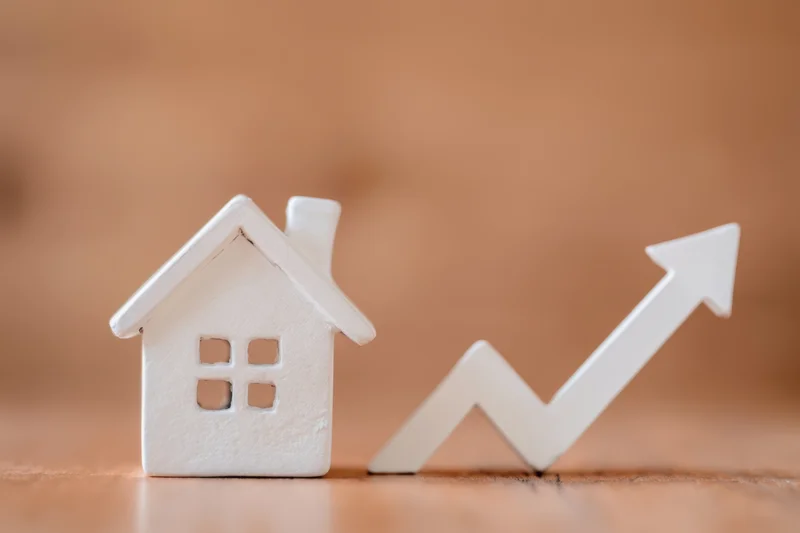 White house figurine next to upward trending arrow on wooden surface