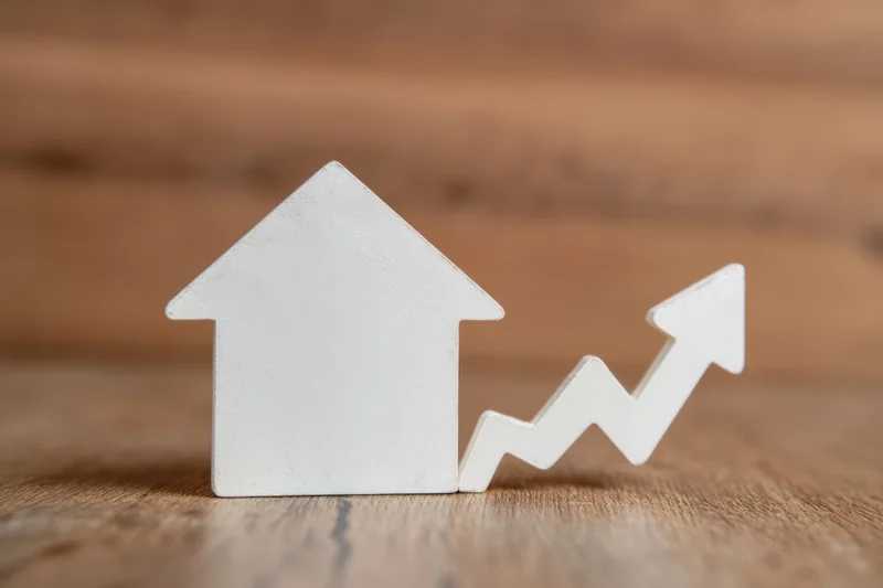 White house figurine next to upward trending arrow on wooden surface