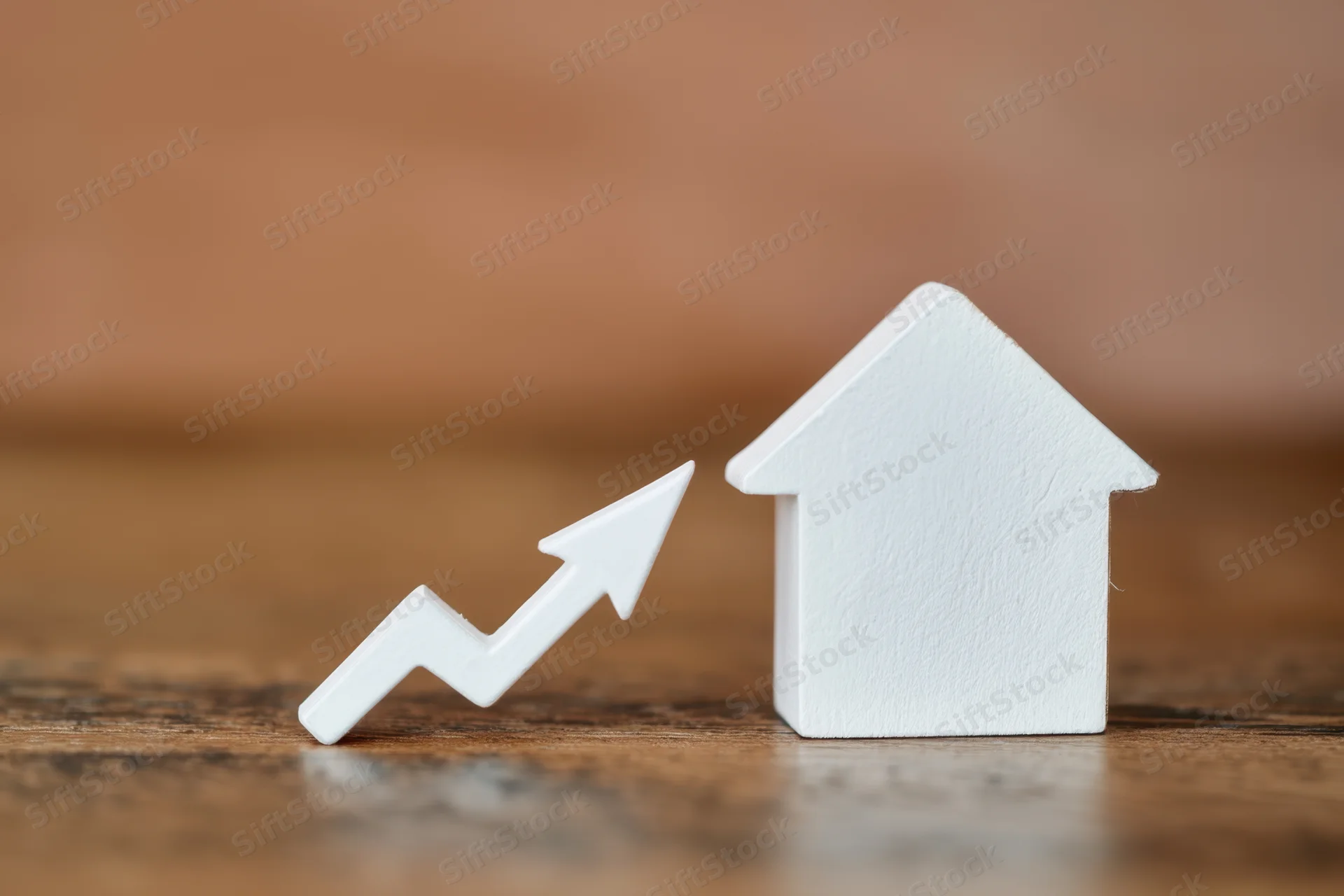 White house figurine next to upward trending arrow on wooden surface