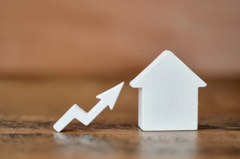White house figurine next to upward trending arrow on wooden surface