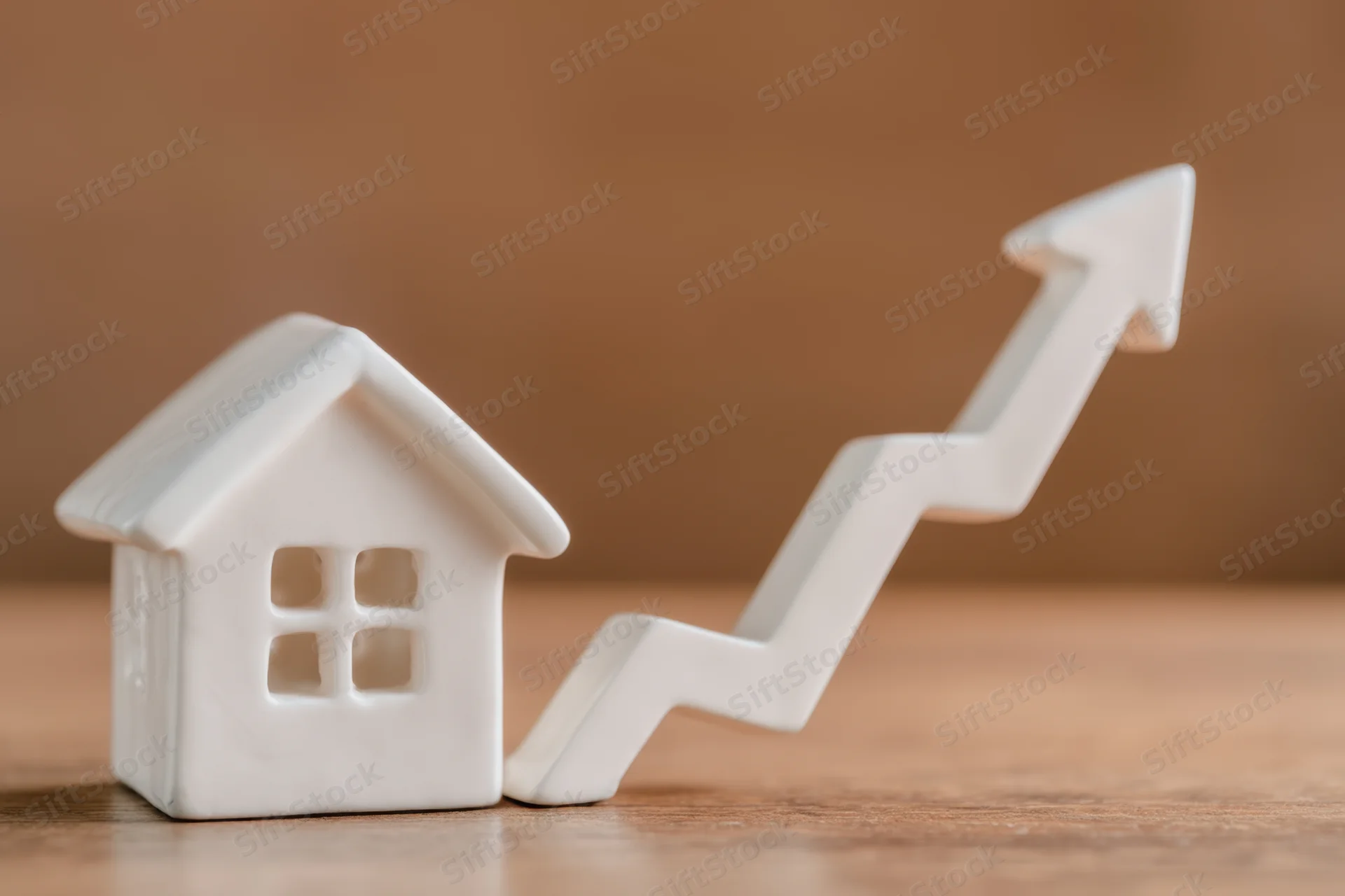 White house figurine next to upward trending arrow on wooden surface