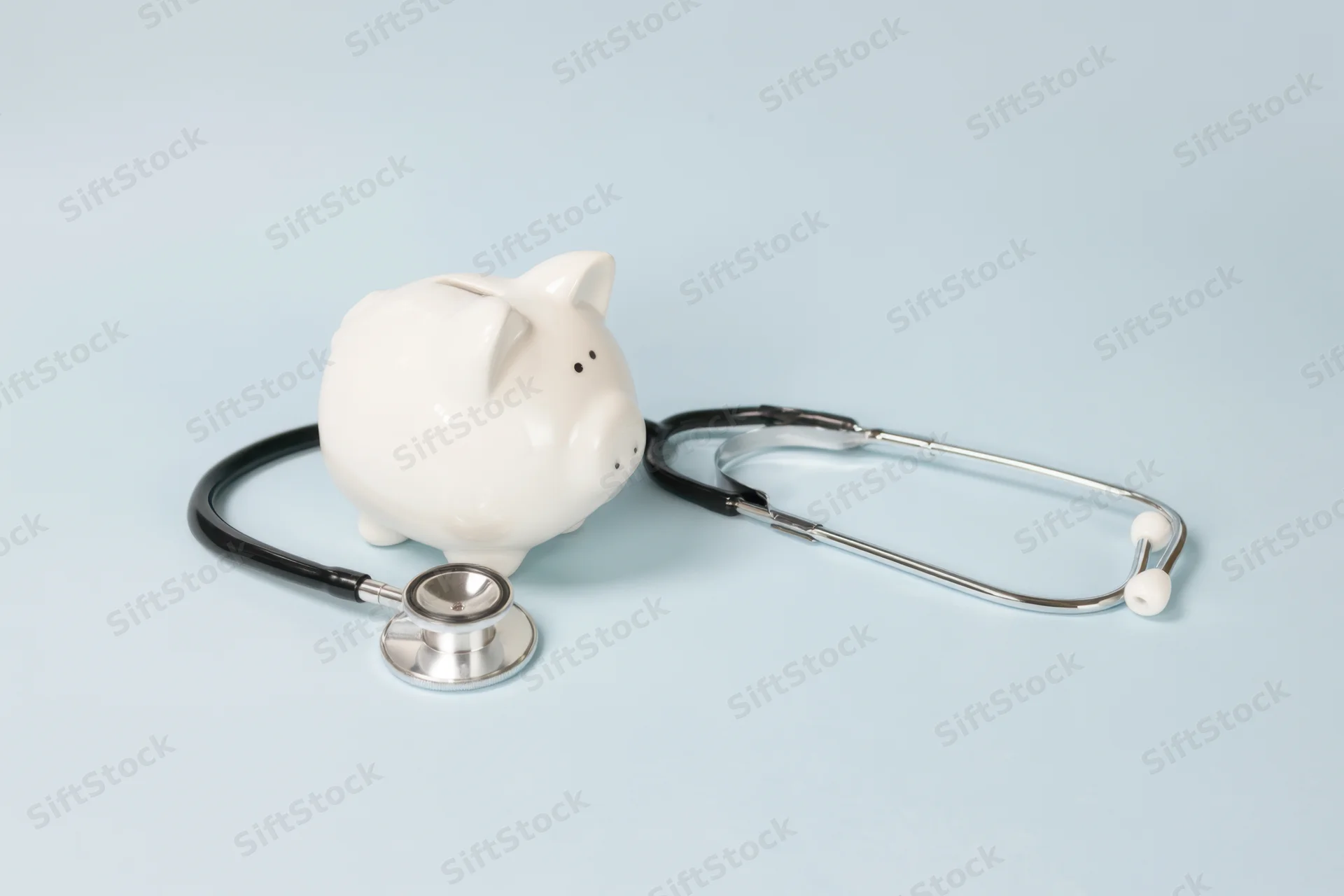 White piggy bank with stethoscope arranged on soft blue surface