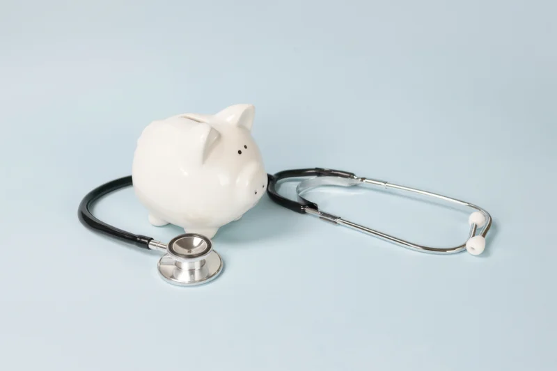 White piggy bank with stethoscope arranged on soft blue surface