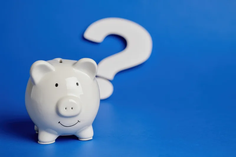 White ceramic piggy bank with smiling face and question mark behind it on blue surface