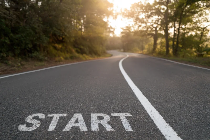 Winding asphalt road with white line and start text at dawn in forested area