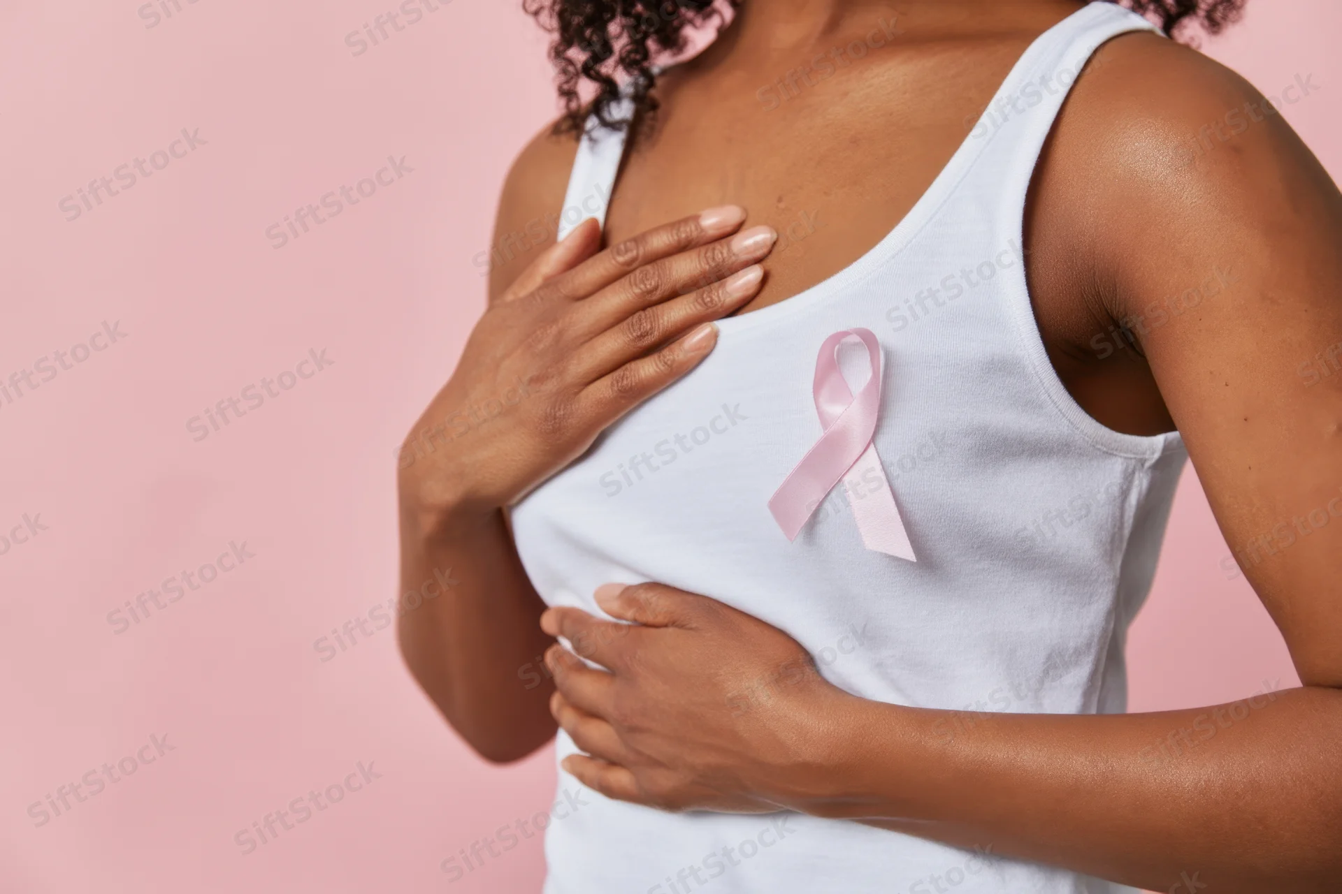 Woman in white tank top touching her chest with pink ribbon pinned to garment