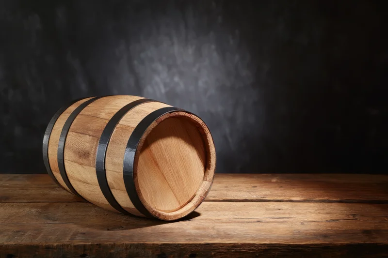 Wooden barrel resting on rustic wooden table with dark textured backdrop