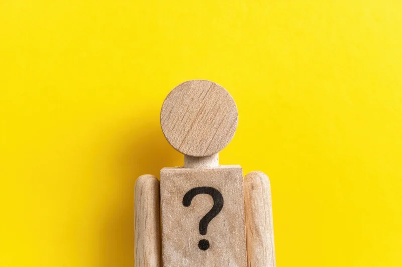 Wooden figure with question mark on torso against yellow background