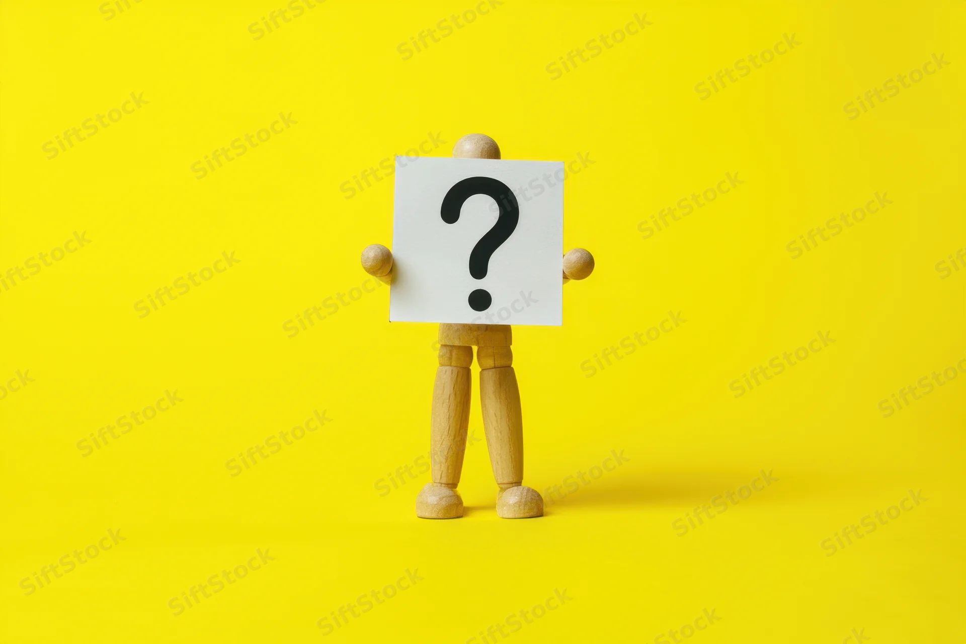 Wooden figure holding a sign with a question mark against a yellow background