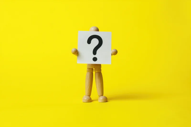 Wooden figure holding a sign with a question mark against a yellow background
