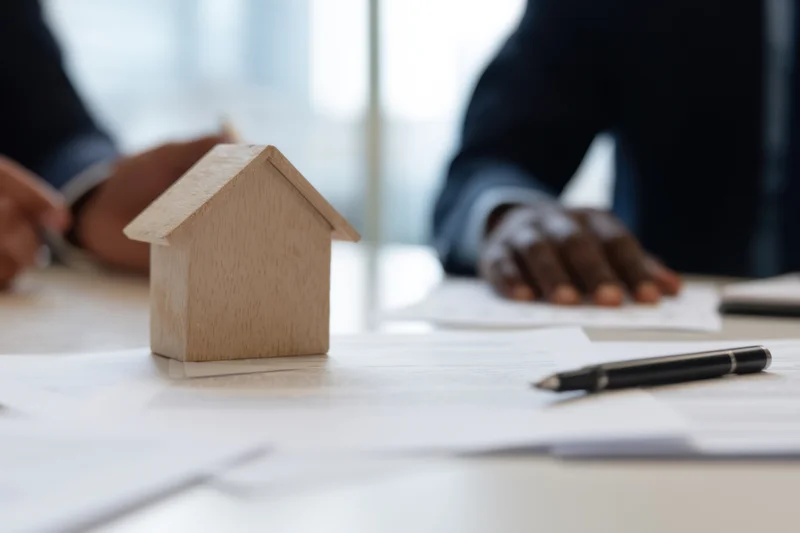 Wooden house model on desk with documents and pen during real estate meeting