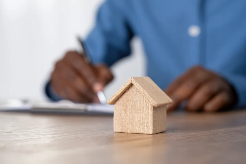 Wooden miniature house on desk with person writing on document in background