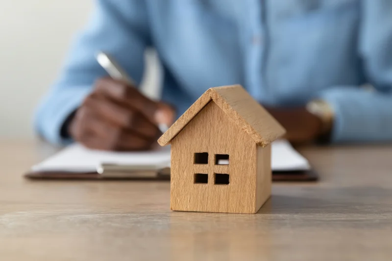 Wooden miniature house on desk with person writing on document in background