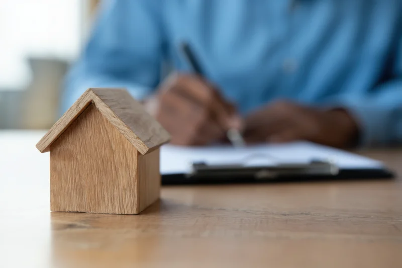 Wooden miniature house on desk with person writing on document in background
