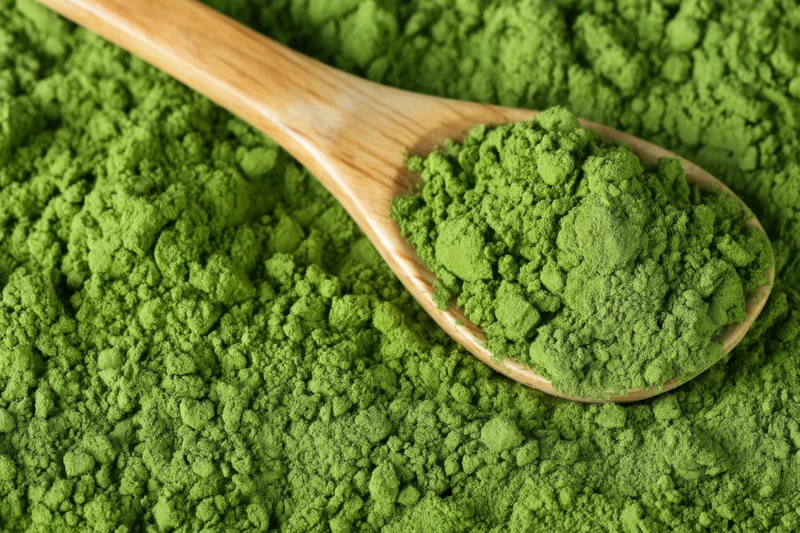 Wooden spoon filled with vibrant green matcha powder resting on a pile of the same powder