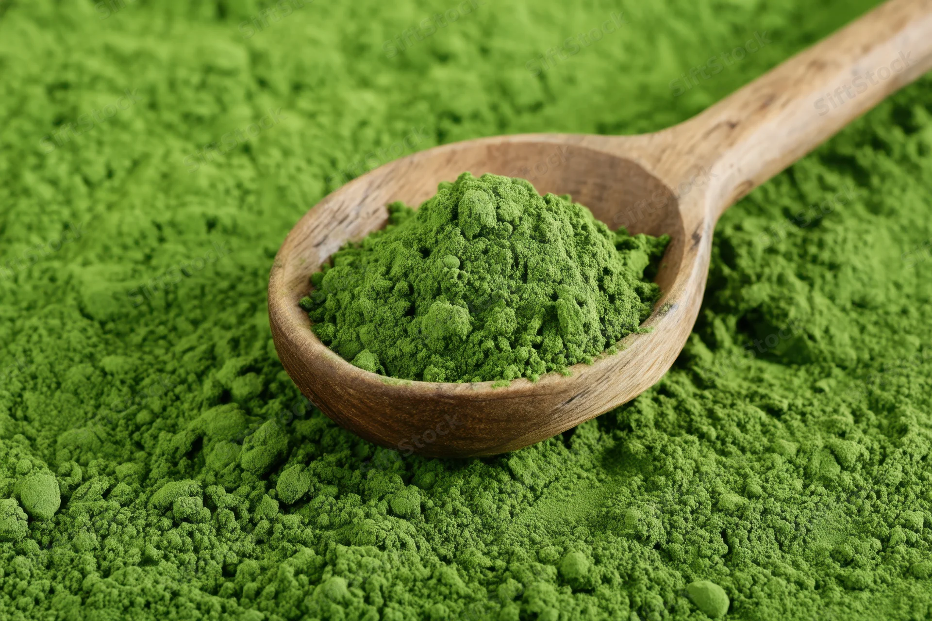Wooden spoon filled with vibrant green matcha powder resting on a bed of the same powder