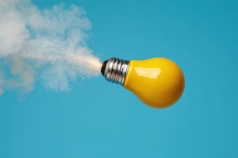 Yellow lightbulb launching like a rocket with smoke against blue background