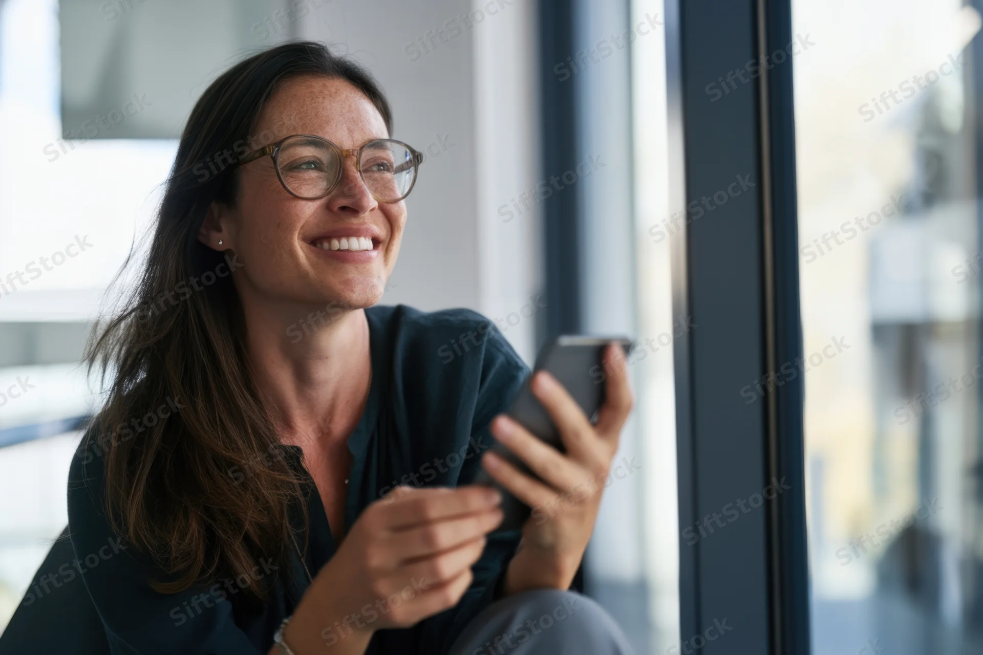 Woman smiling while using smartphone in modern office near window