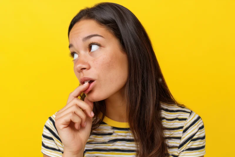 Young hispanic woman with thoughtful expression biting her lip against yellow background