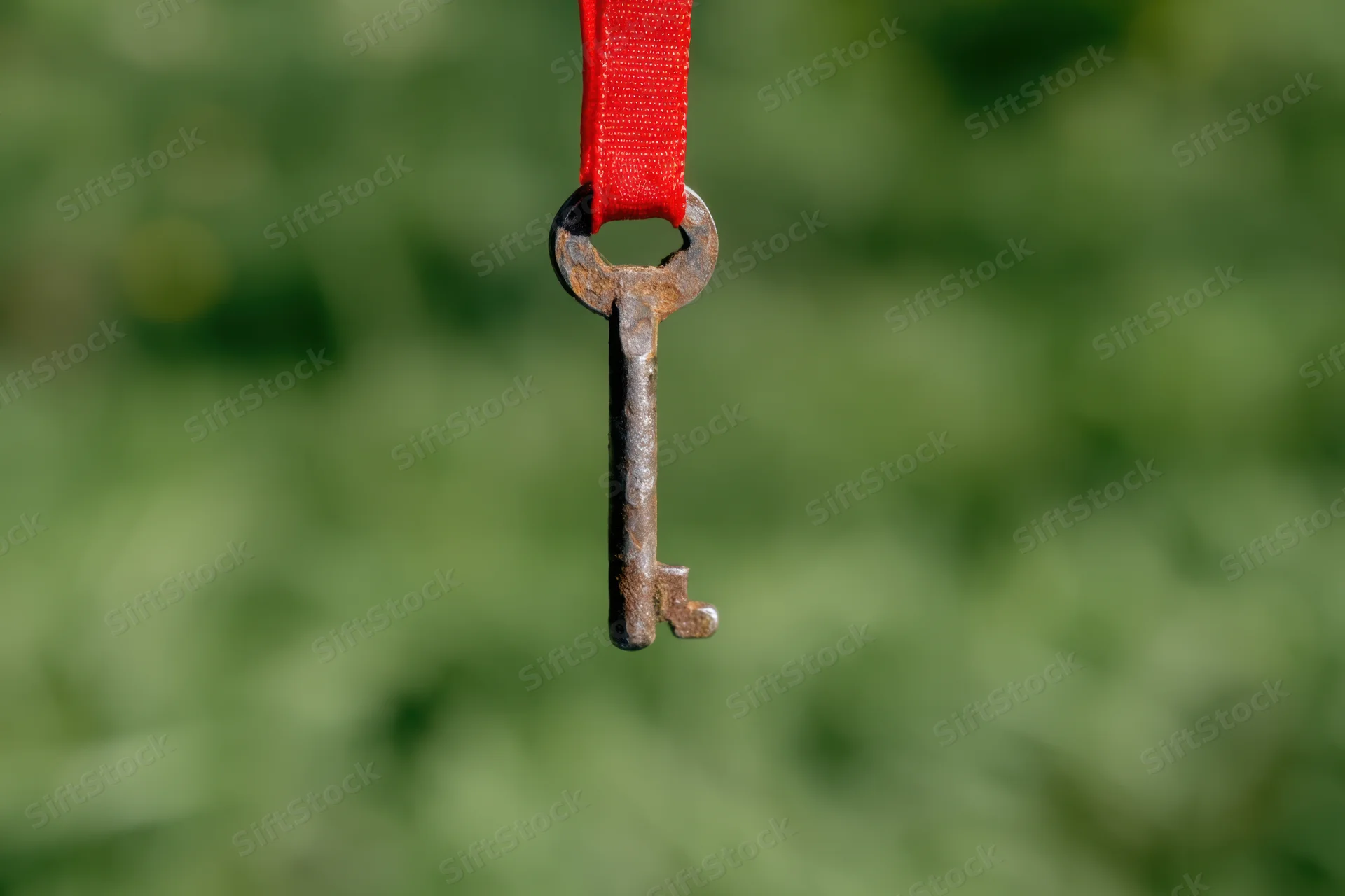 Antique rusted key hanging from red ribbon against blurred green background