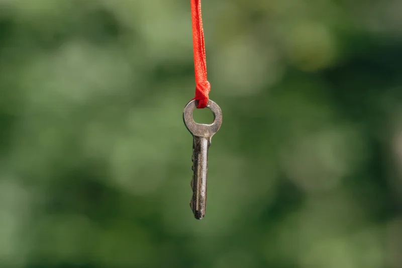 Antique key hanging from red ribbon against blurred green background