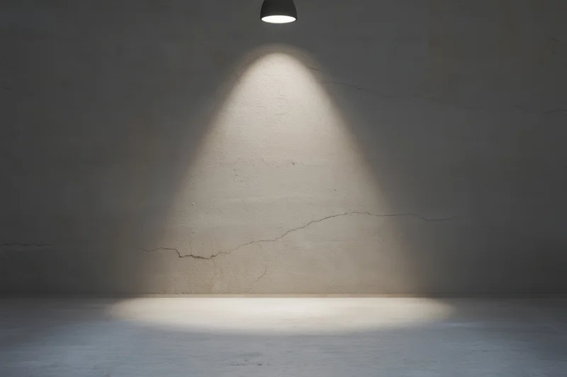 Spotlight illuminating cracked concrete wall in empty dim room