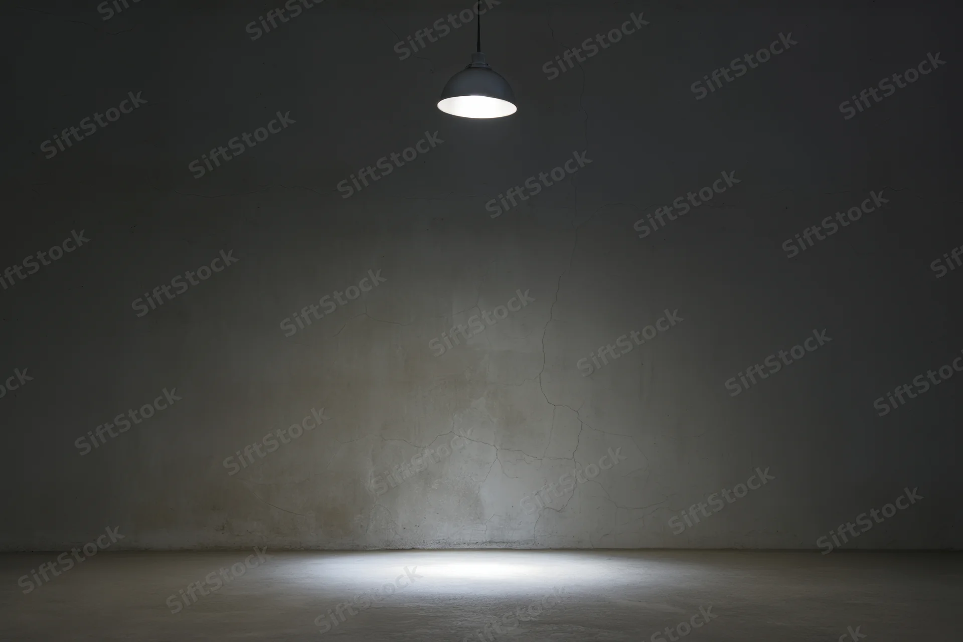Empty dimly lit room with cracked concrete wall and pendant lamp casting spotlight on floor