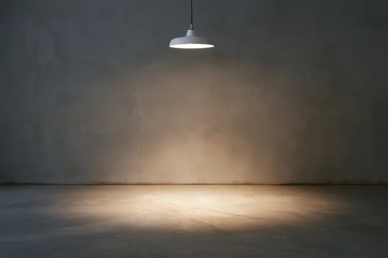 Pendant light hanging over empty concrete room with cracked wall and illuminated floor