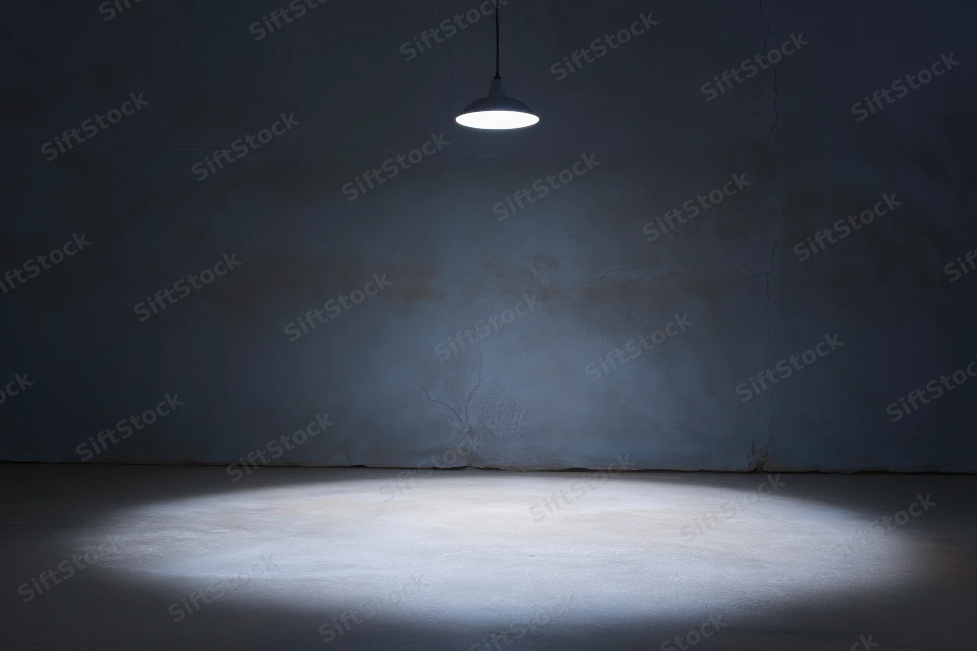 Dimly lit empty room with cracked concrete wall and pendant lamp casting spotlight on floor