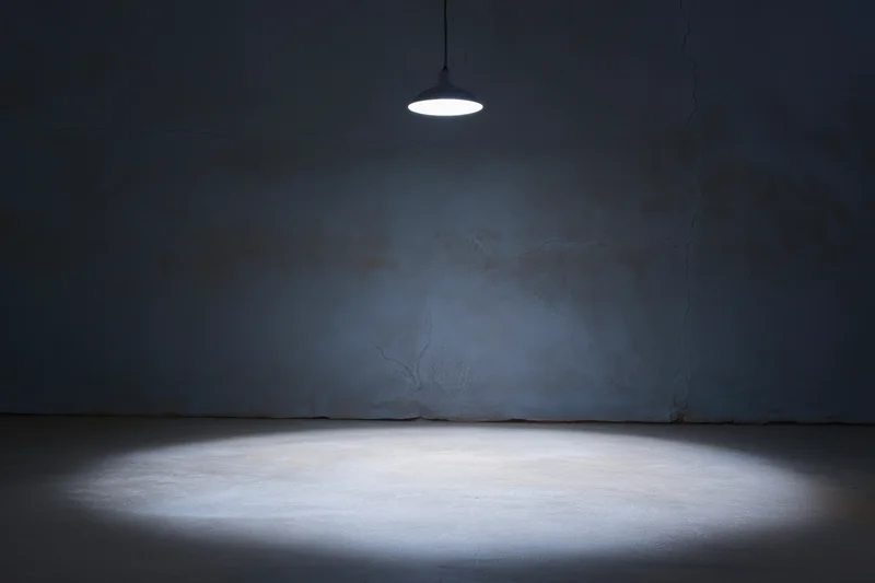 Dimly lit empty room with cracked concrete wall and pendant lamp casting spotlight on floor