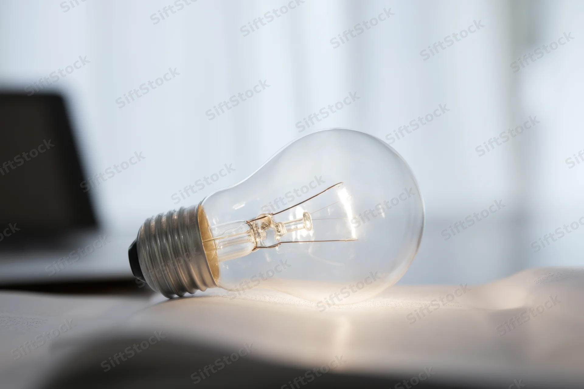 Illuminated lightbulb resting on open book with laptop in background