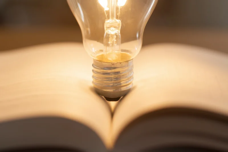 Lightbulb glowing above open book pages with warm illumination