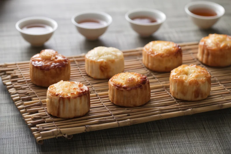 Mooncakes arranged on a bamboo mat with tea cups nearby