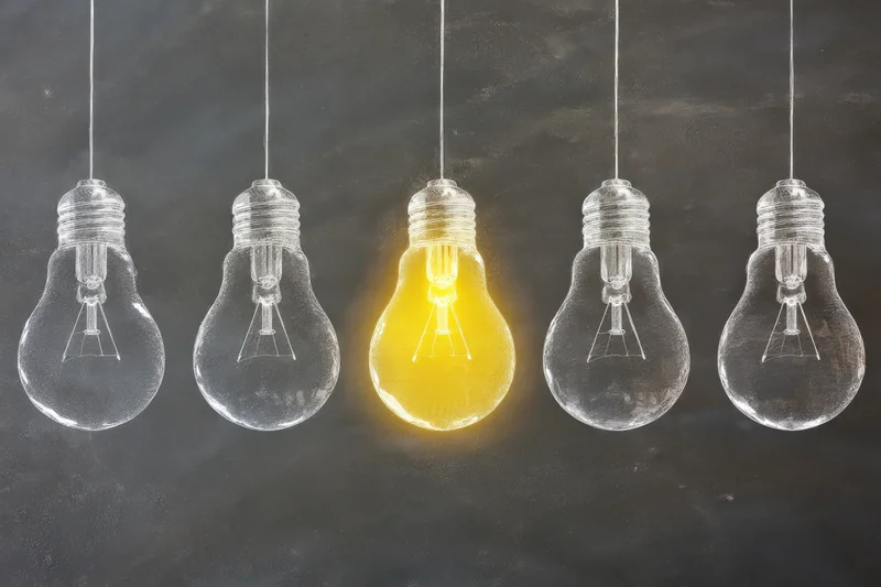 Five hanging lightbulbs with one illuminated on a chalkboard background