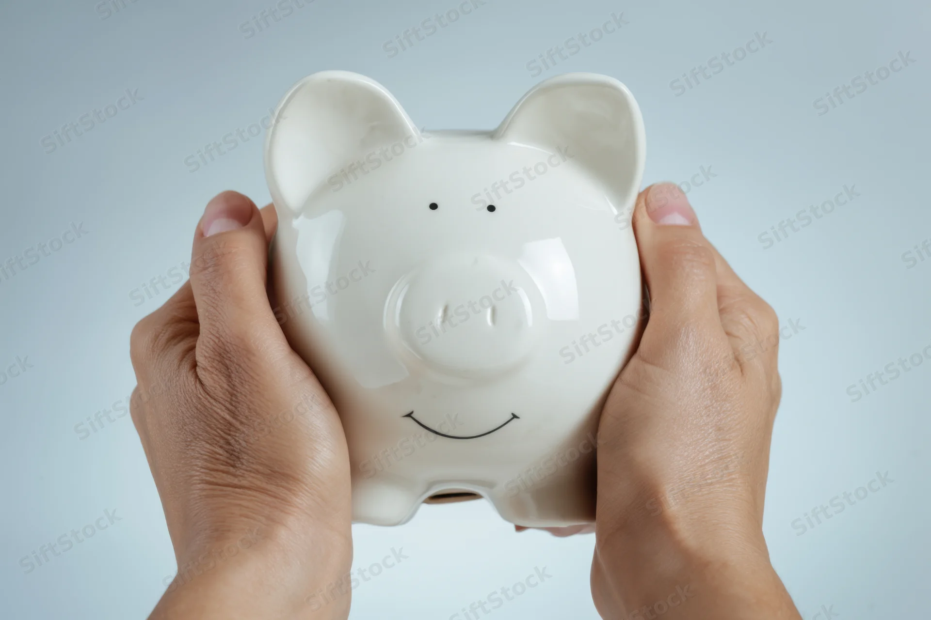 Hands gently holding a white ceramic piggy bank against a light neutral background