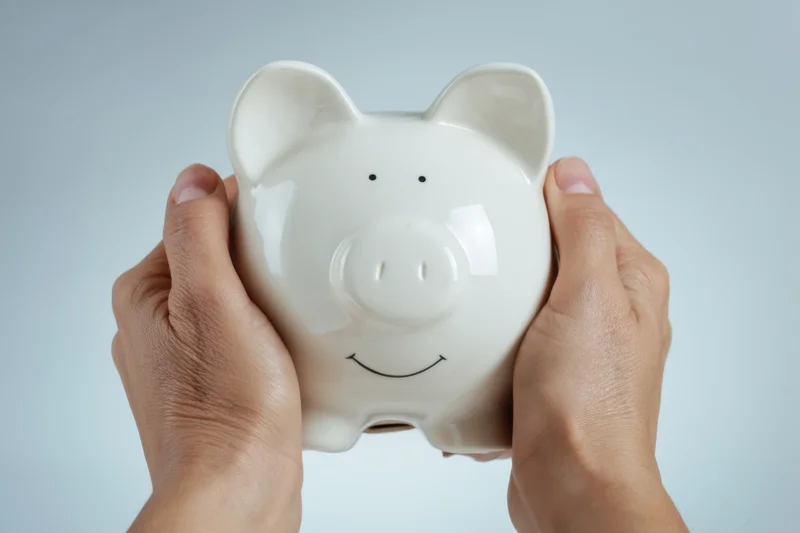 Hands gently holding a white ceramic piggy bank against a light neutral background
