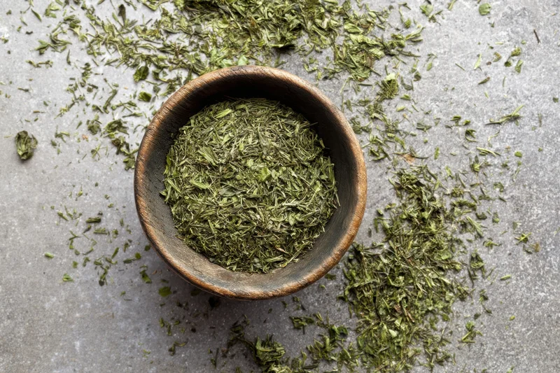 Loose green tea leaves in a rustic wooden bowl scattered on a gray stone surface