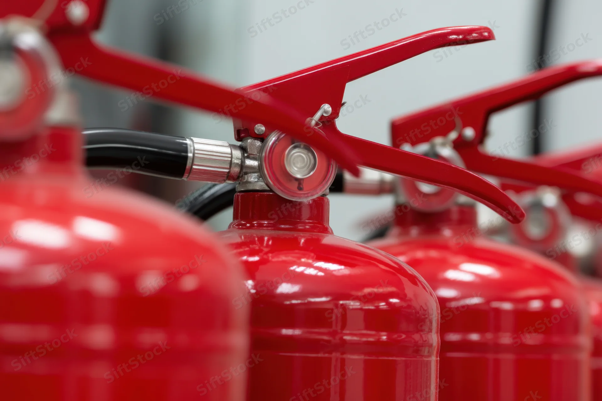 Multiple red fire extinguishers arranged in a row showing handles and nozzles in closeup view