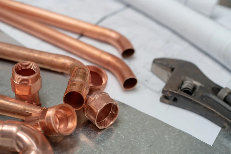 Copper plumbing pipes and fittings with wrench arranged on a work surface over blueprints