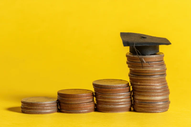 Stacks of coins increasing in height with a graduation cap on the tallest stack against a yellow background