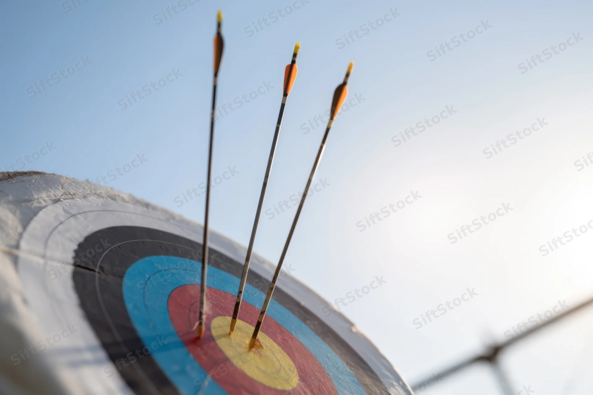 Three arrows embedded in the center of a colorful archery target under a clear sky