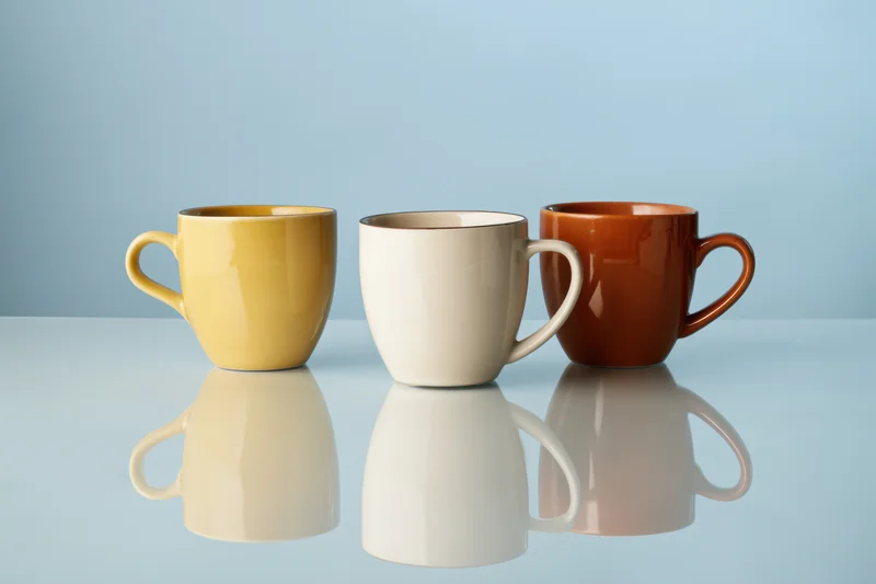 Three colorful ceramic coffee mugs arranged in a row on a reflective blue surface