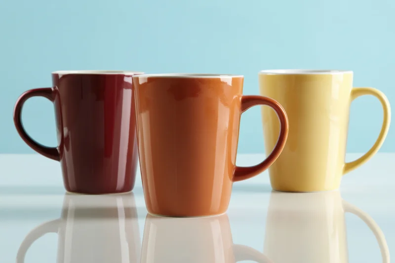 Three colorful ceramic coffee mugs arranged in a row on a reflective blue surface