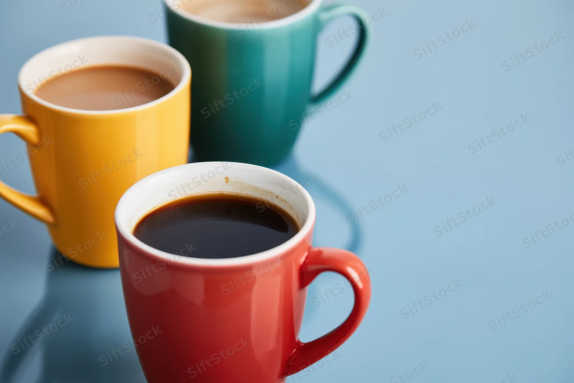 Three colorful coffee mugs arranged on a blue surface with copyspace