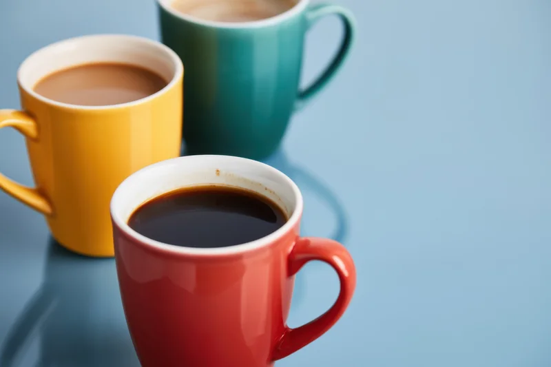 Three colorful coffee mugs arranged on a blue surface with copyspace